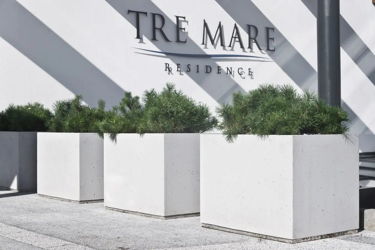 White concrete planters with green plants in front of a building with 'Tre Mare Residence' sign.