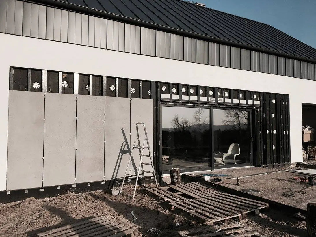 Modern house under construction with large concrete wall panels, glass doors, and visible building materials.