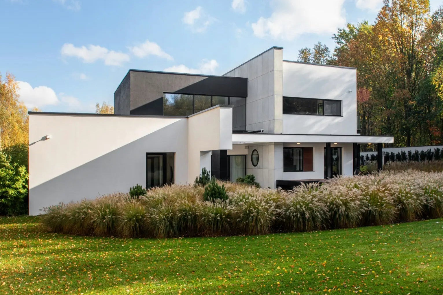 Modern white house with geometric design and concrete wall panels  in a green landscape