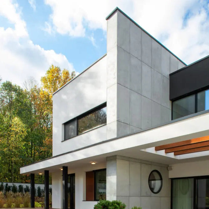 Modern house exterior with concrete wall panels, a wooden deck, and a garden area.