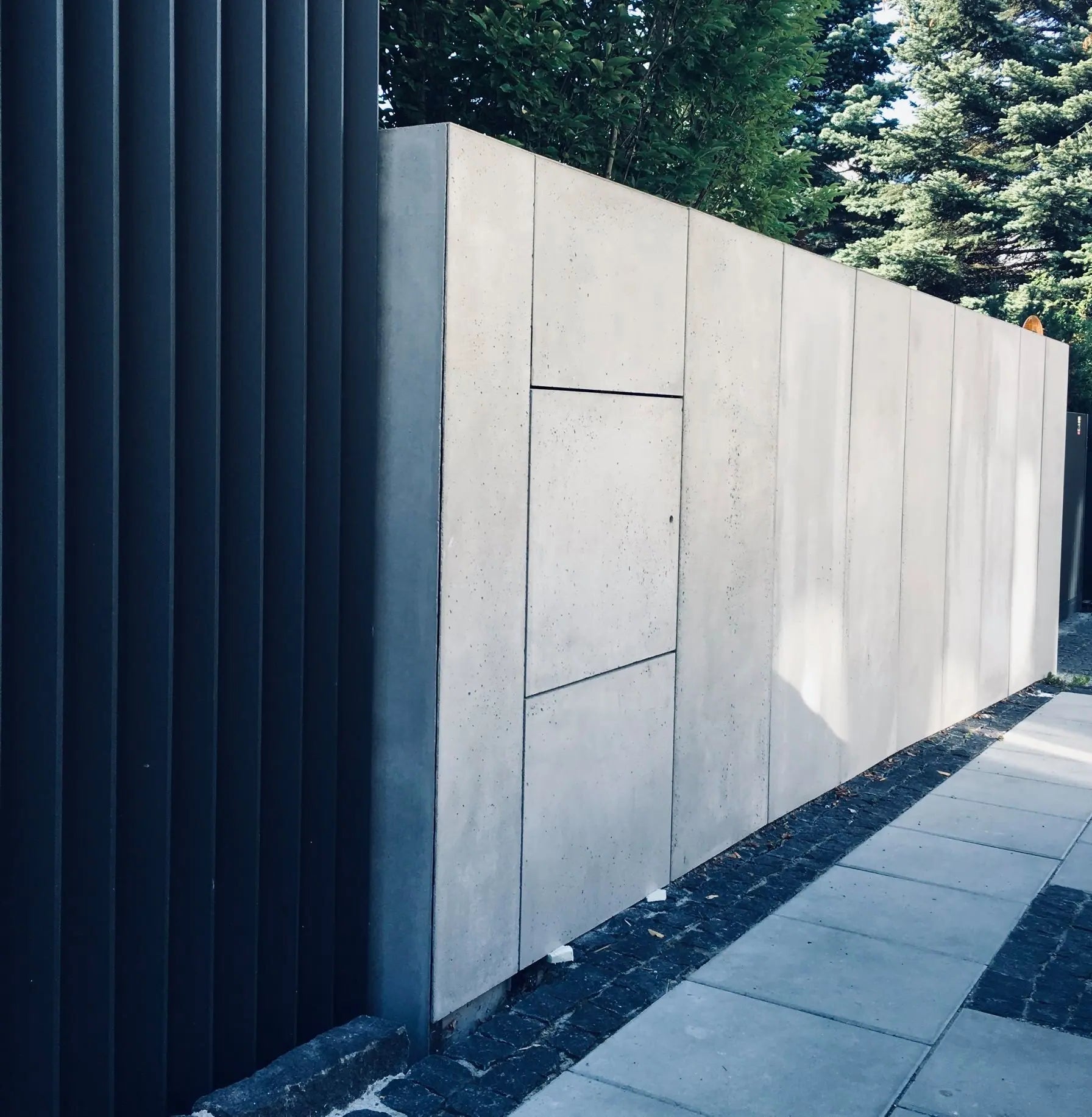 Modern concrete wall with a dark metal panel in an outdoor setting