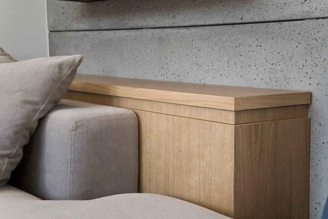 Wooden headboard with a textured concrete  wall and grey sofa in the background