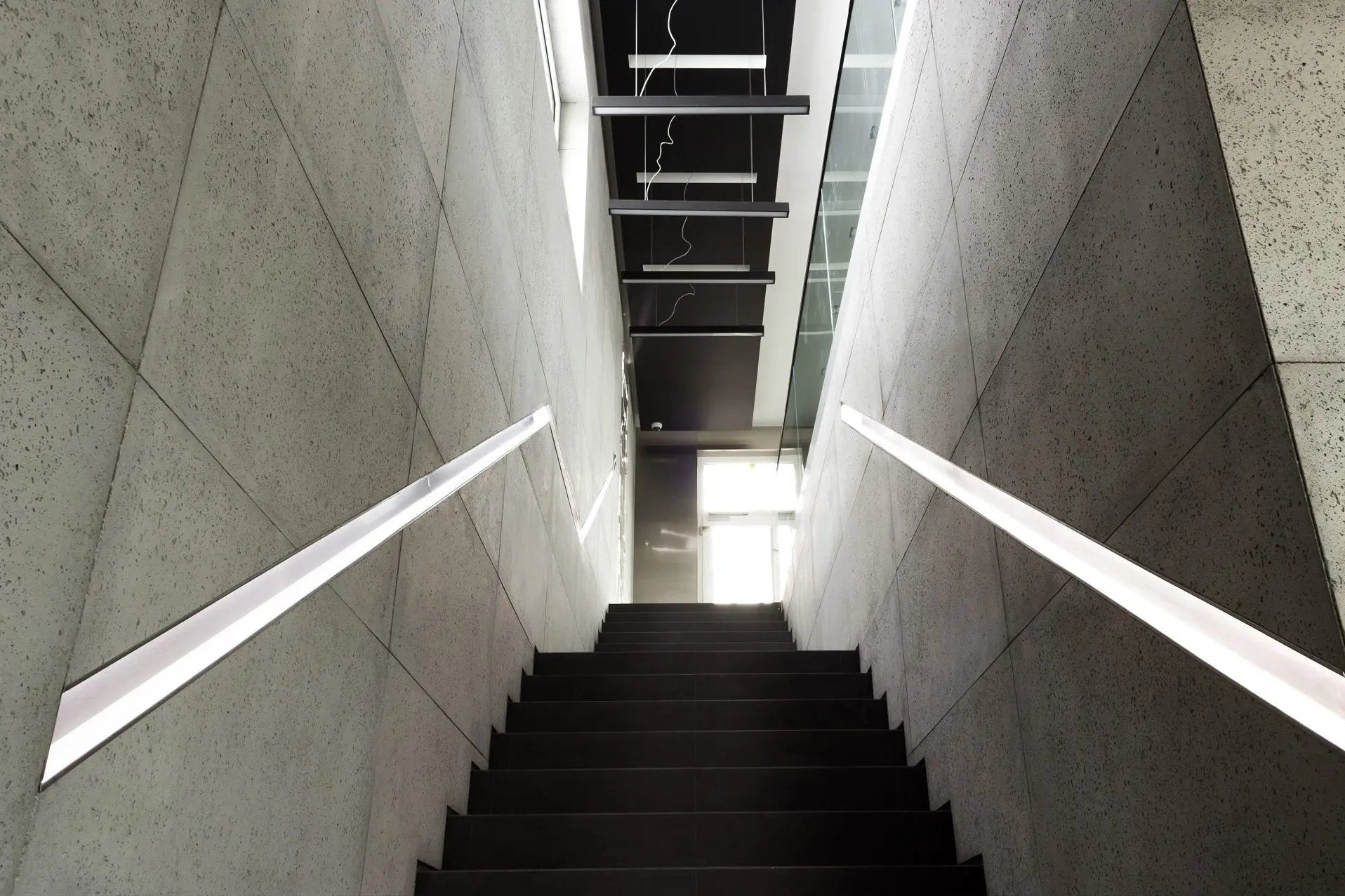 Modern staircase with concrete walls and a light fixture in an indoor setting.