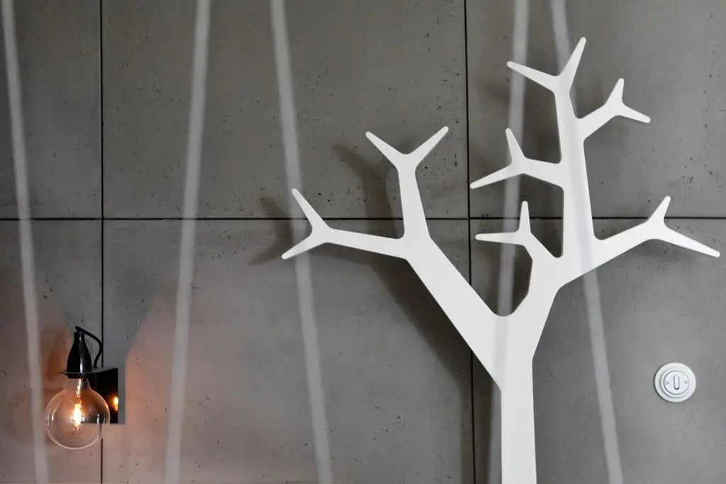White tree-shaped coat rack on a gray concrete wall with a light fixture.