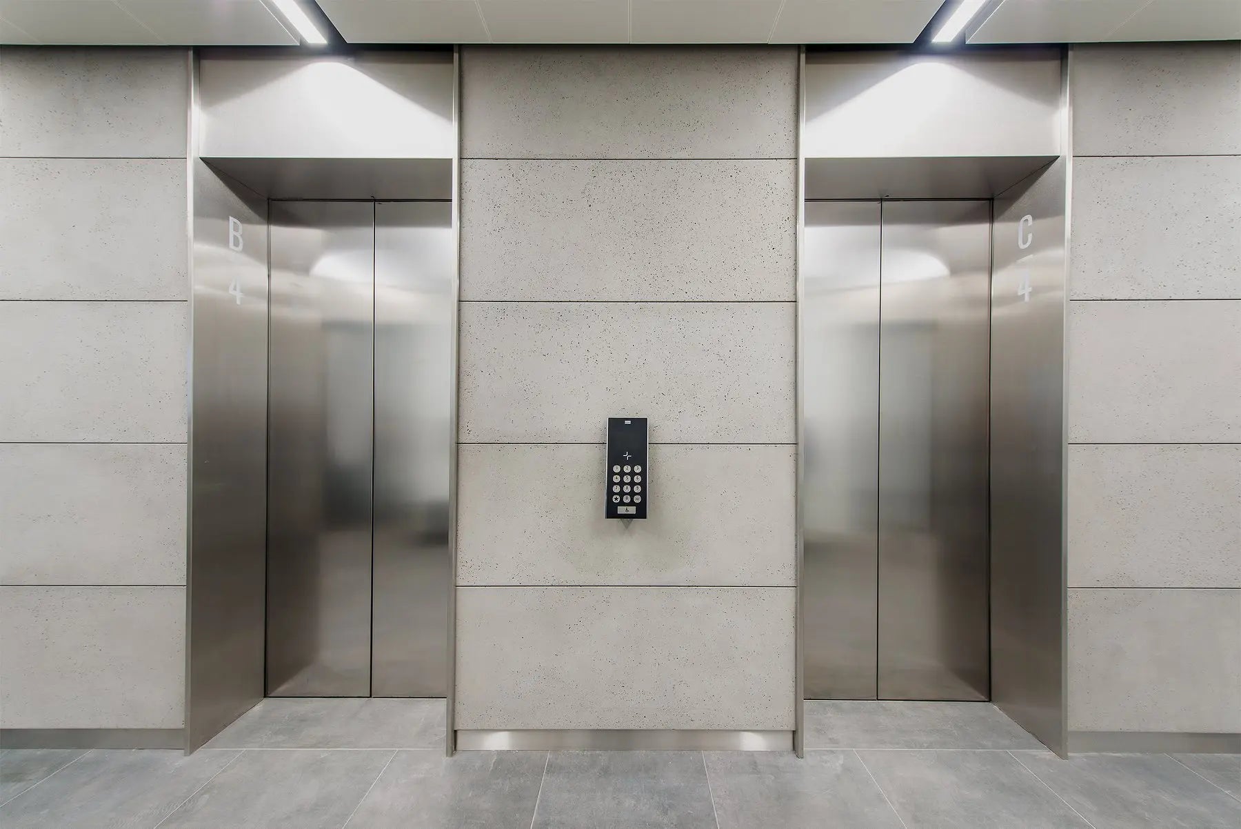 Elevator doors with a control panel in a modern building, with concrete panelling on the interior.