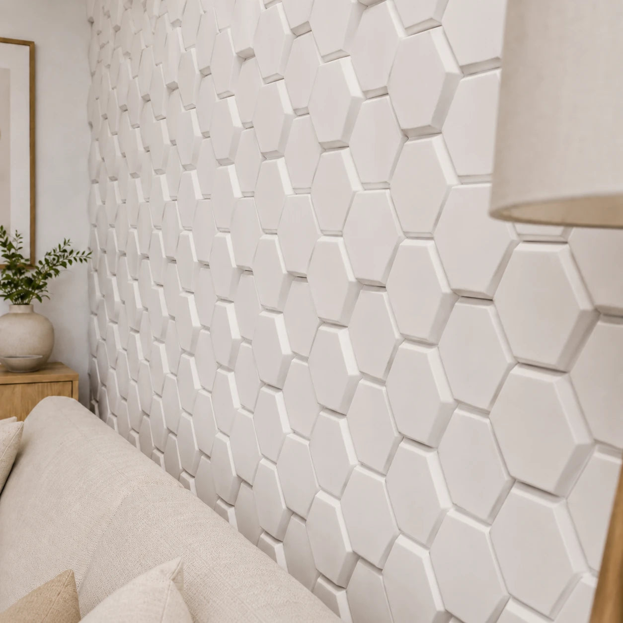 Close-up angled view of white convex hexagonal wall panels, highlighting their raised depth, beveled edges, smooth polystyrene surface, and honeycomb arrangement, with part of the sofa and lamp visible for scale