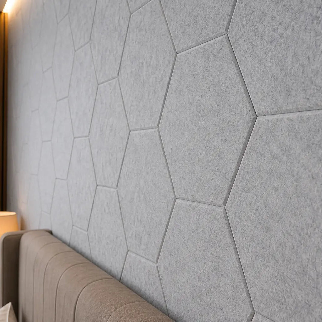 Grey HEXA 3D felt PET wall panels in a contemporary bedroom with a large upholstered bed, wooden furniture and warm bedside lighting close up view