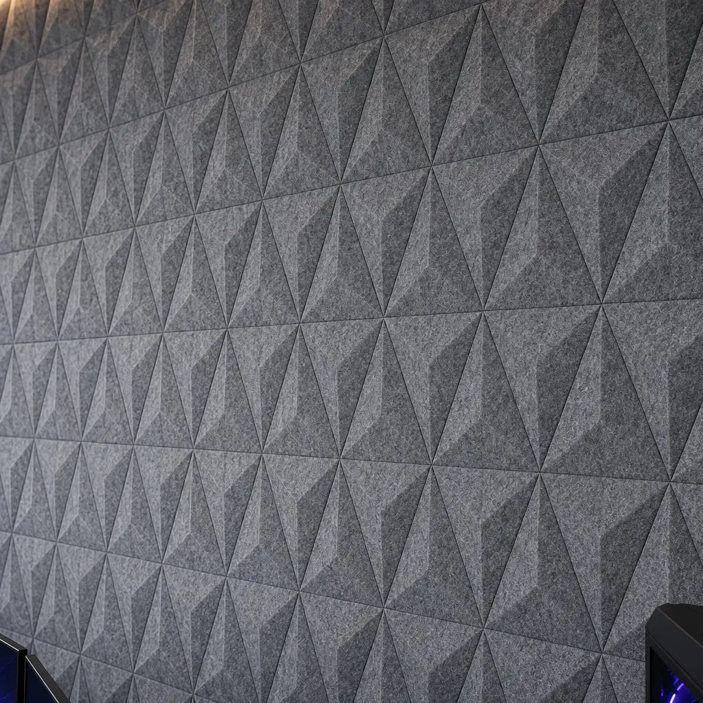Close-up of grey PYRAMID 3D acoustic felt wall panels at a 45-degree angle, showing their geometric pattern, subtle relief and textured PET felt surface