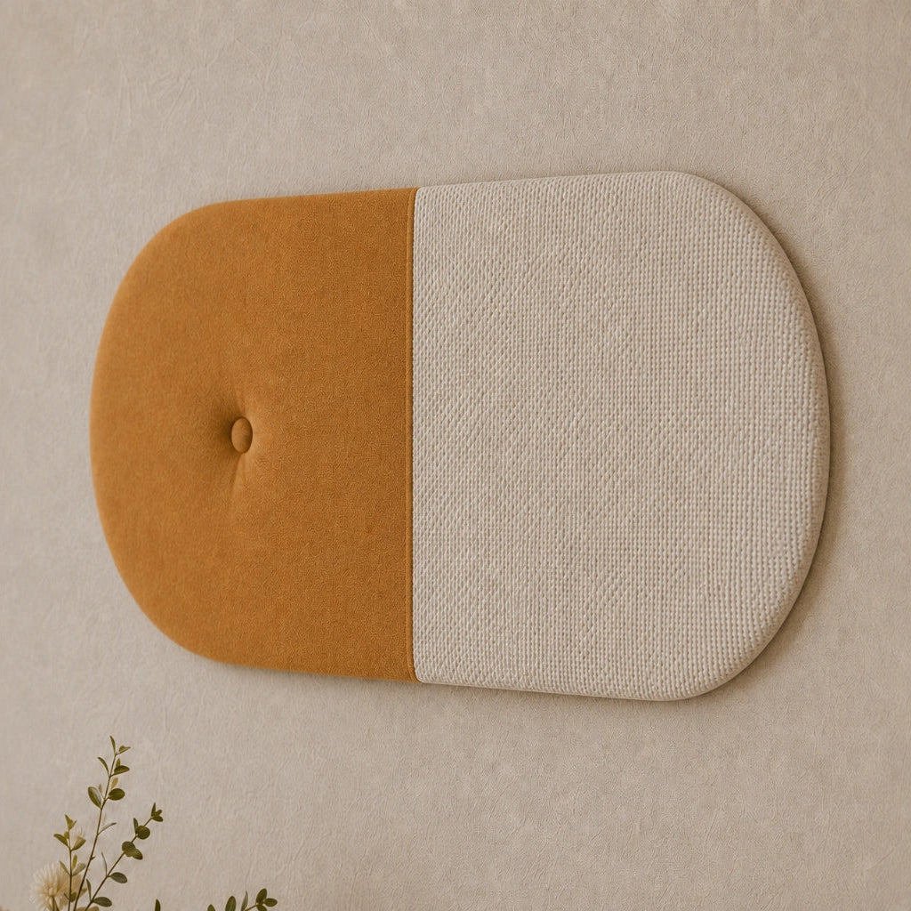 Close-up angled view of a two-tone upholstered wall panel, highlighting its mustard fabric, textured cream section, rounded shape, central seam and button detail.