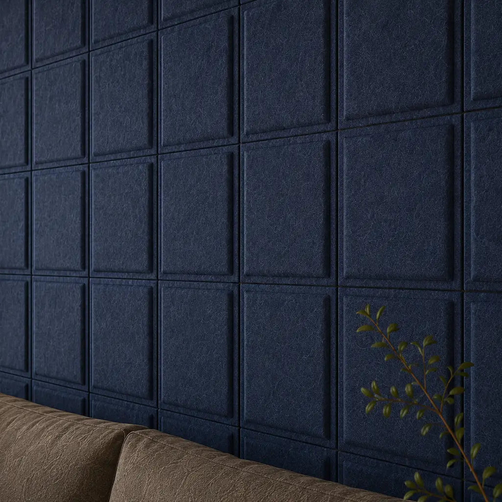 Close-up of navy Square Bold 3D acoustic felt panels behind a taupe sofa, with plants and warm lighting