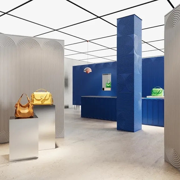 Boutique interior with grey arched wall panels, a blue textured column and colourful handbags on display