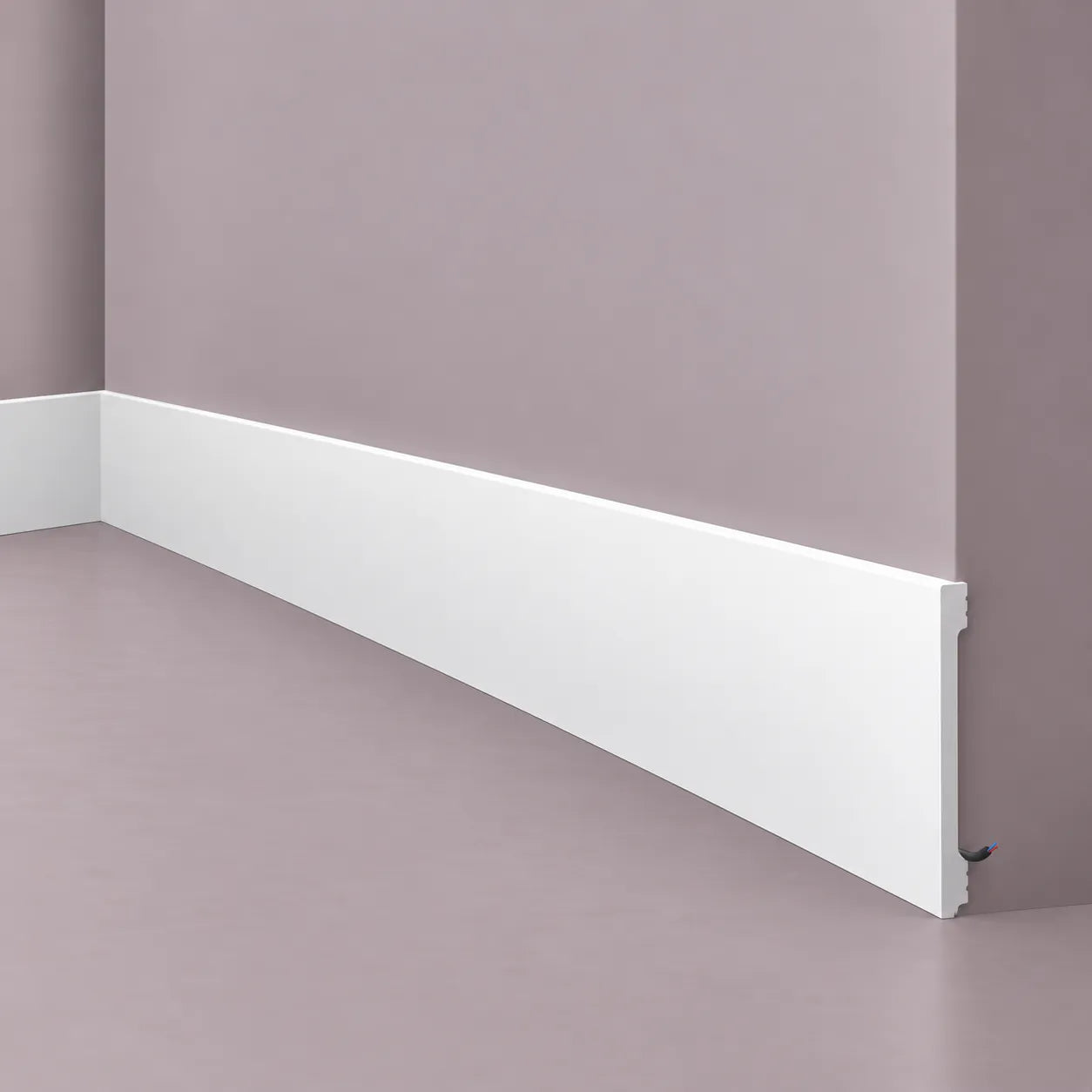 White NMC F20S skirting profile with integrated cable channel, shown installed around an interior wall corner