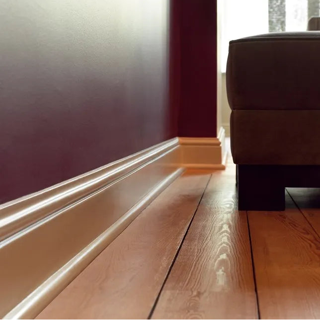 Close-up of decorative white skirting board installed against a dark feature wall with warm natural wood flooring