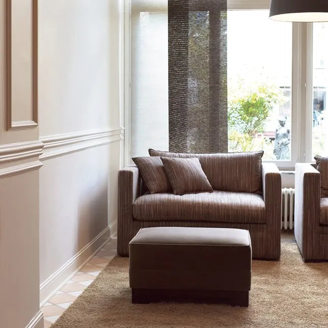 Elegant living room with white decorative skirting and wall mouldings, neutral upholstered seating and a large window with natural daylight