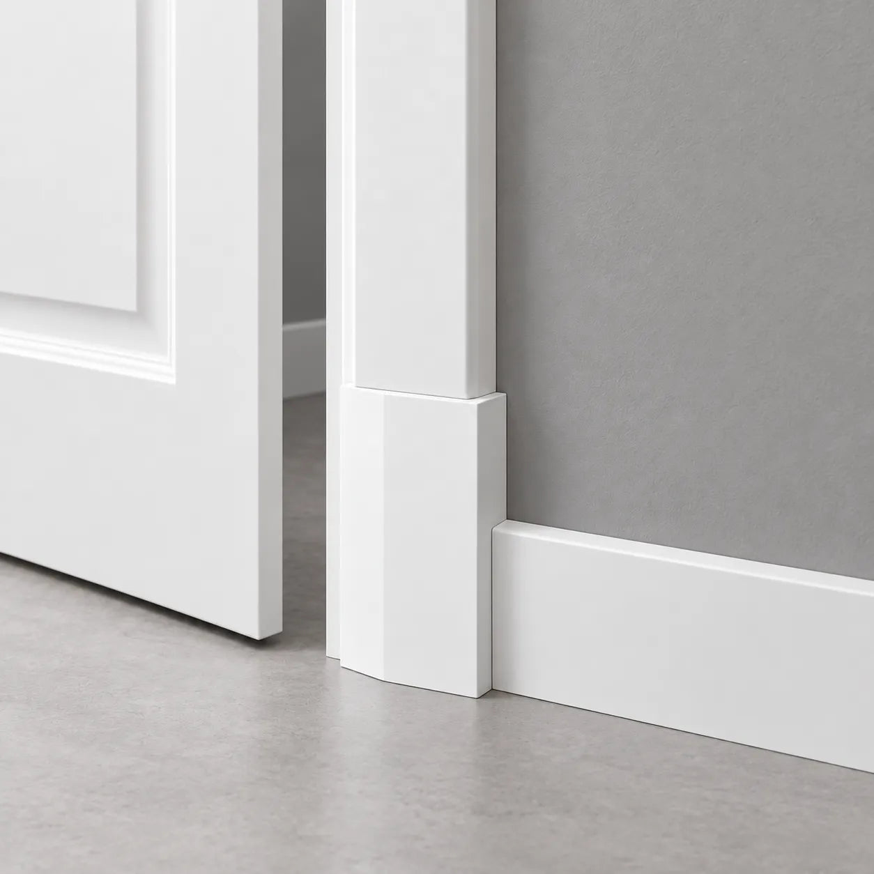 White WB2 WALLSTYL plinth block joining a door architrave and skirting board beside an ajar door in a grey room