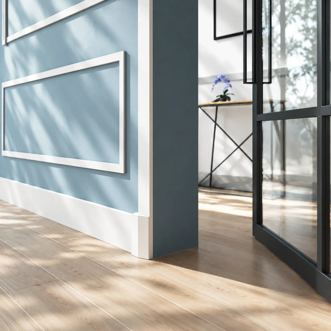Angled view of a white WB2 WALLSTYL plinth block at the base of a blue doorway beside an open black framed glass door